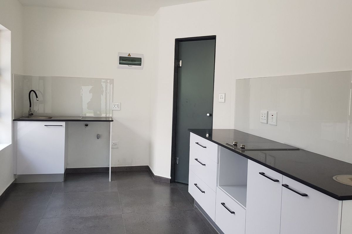 A modern, clean kitchen featuring white cabinetry, dark stone countertops, integrated hob, and a glass splashback in a bright, minimalist space.