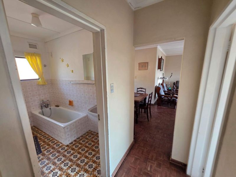 A view from the hallway looking into a bathroom with a built-in tub and adjacent living area featuring parquet flooring.