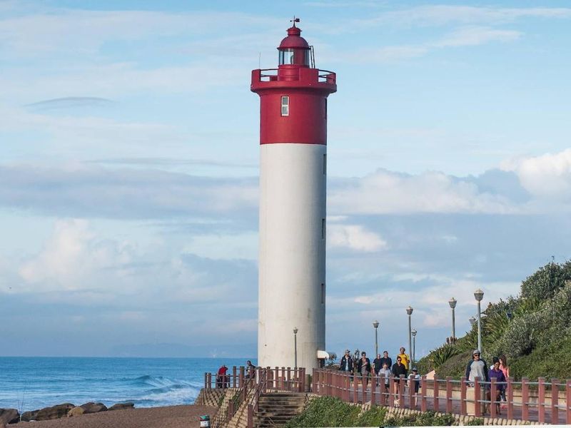 A scenic view of the iconic red and white lighthouse situated along a paved coastal walkway with ocean views.