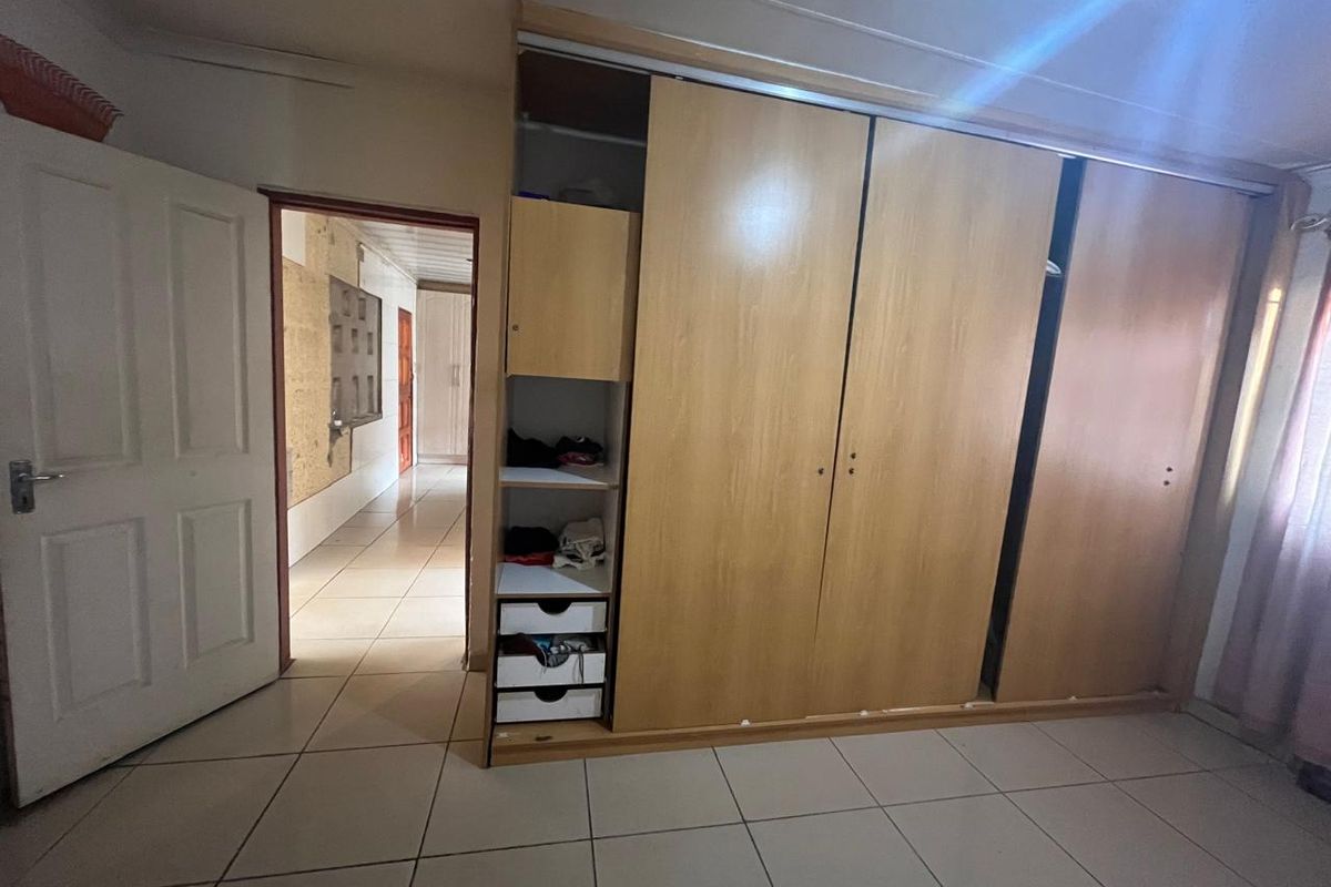 Bedroom featuring built-in wooden wardrobes and tiled flooring, with a view into the adjacent hallway showing visible wall surface damage.