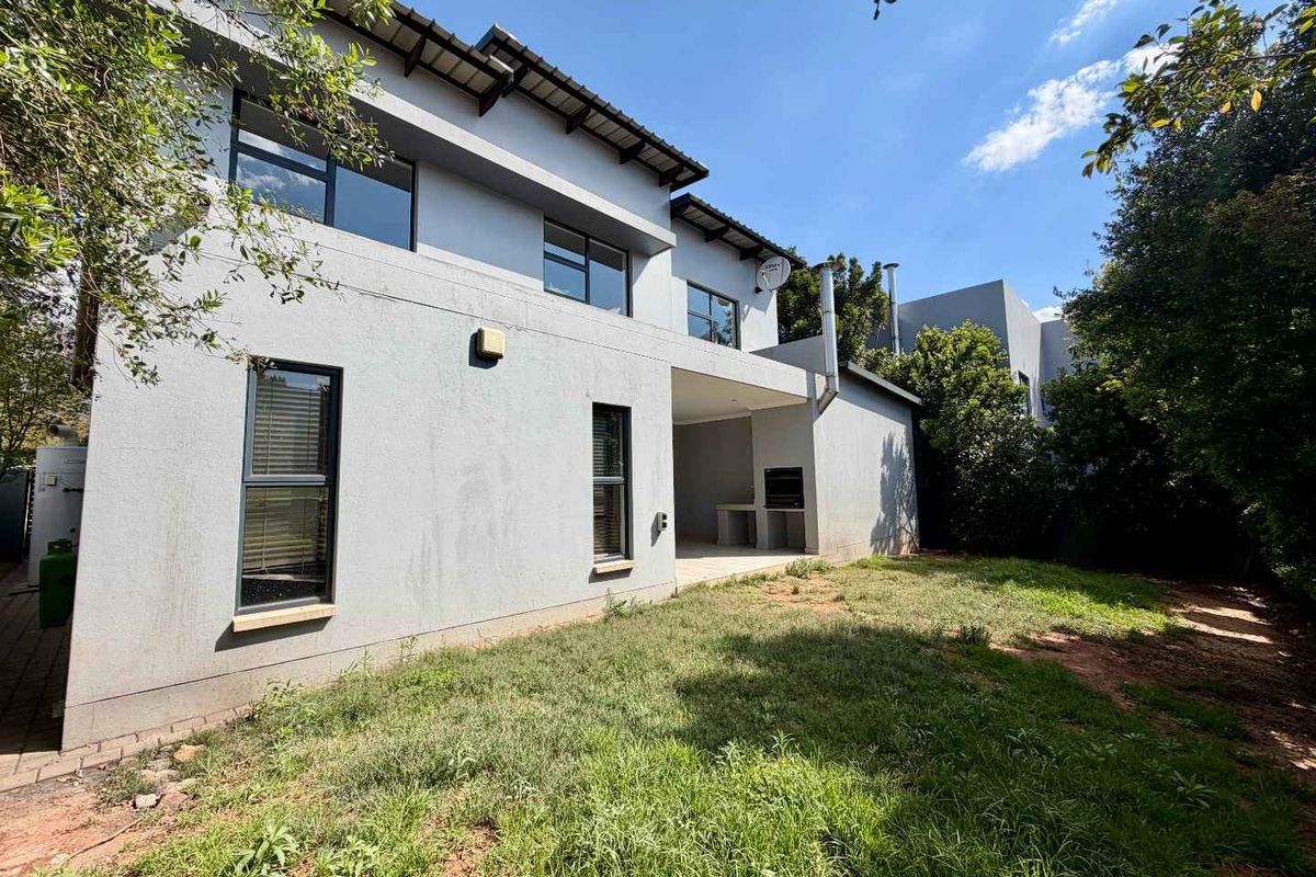 Rear view of the property featuring a covered patio with a built-in braai, overlooking a private garden area.