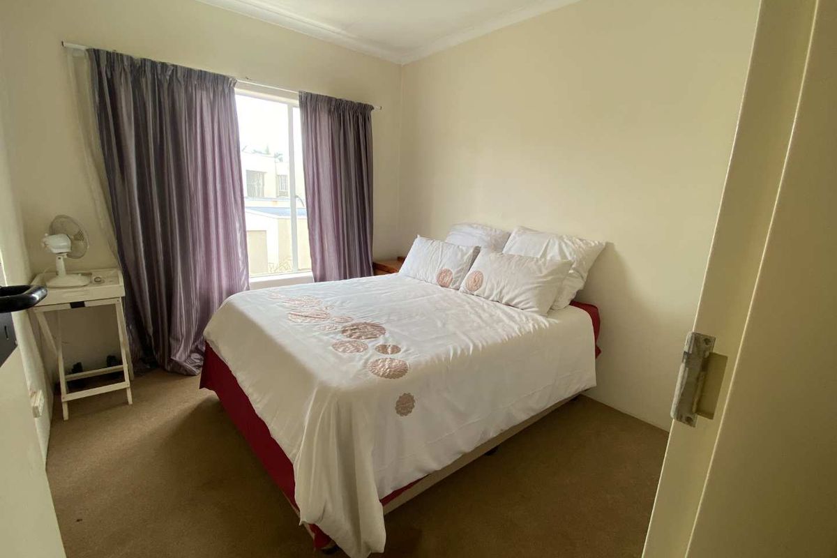 A standard bedroom featuring neutral walls, carpeted flooring, and a window with curtain tracks.