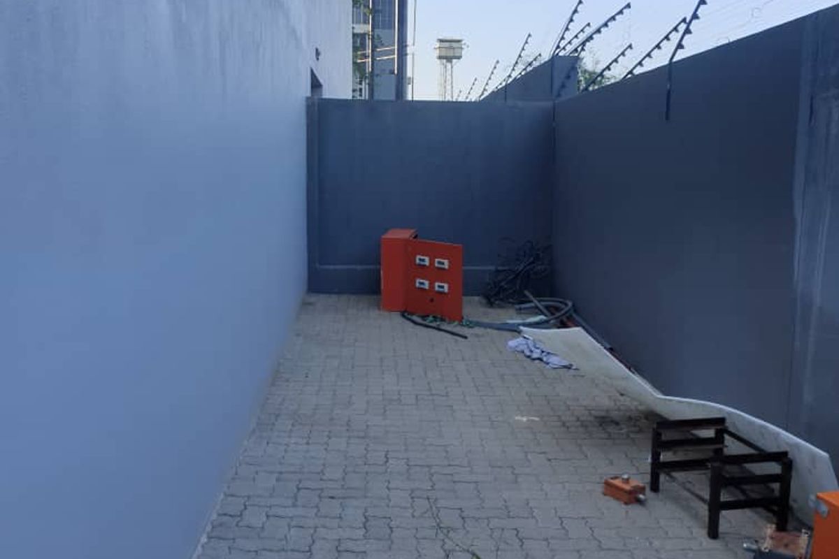 A side exterior utility area featuring paved flooring, perimeter boundary walls, and security electric fencing.
