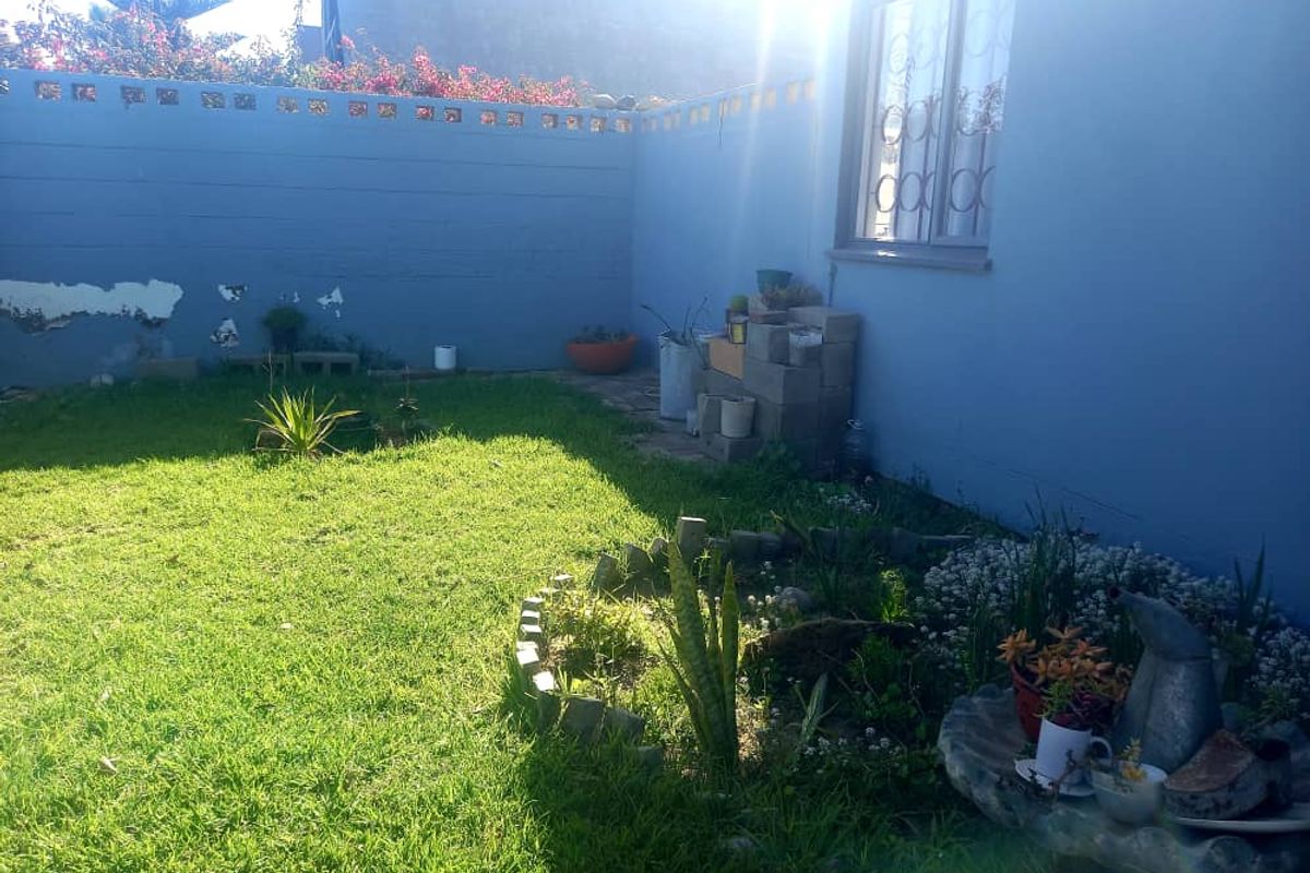 A private rear garden area featuring a lawn, landscaped garden beds, and a perimeter boundary wall with security bars on the window.