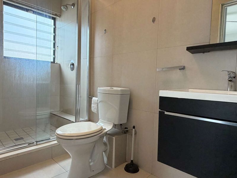 A clean, modern bathroom featuring a glass-enclosed shower, a wall-mounted vanity with a basin, and neutral floor-to-ceiling wall tiles.