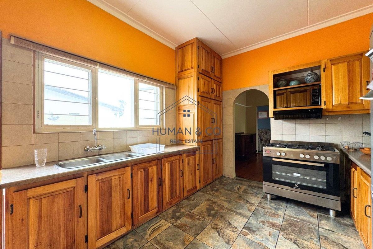 A functional kitchen featuring wooden cabinetry, a built-in gas stove with extractor fan, double sink, and tiled flooring.