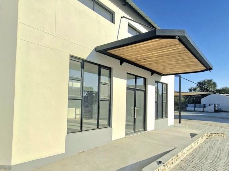Modern office building exterior featuring a contemporary timber-slat canopy, large glass entrance doors, and clean paved frontage.