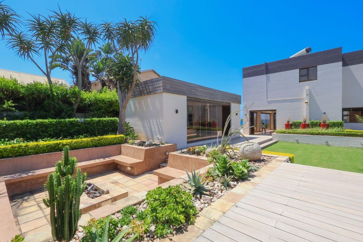A beautifully landscaped rear garden featuring a sunken fire pit area, timber decking, and modern architectural structures with glass sliding doors.