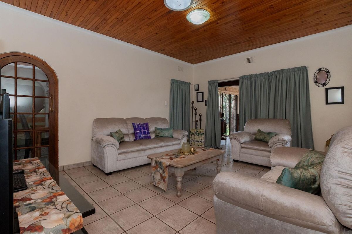 A living room featuring tiled flooring, a timber-paneled ceiling, and an arched wooden door leading to an adjacent space.