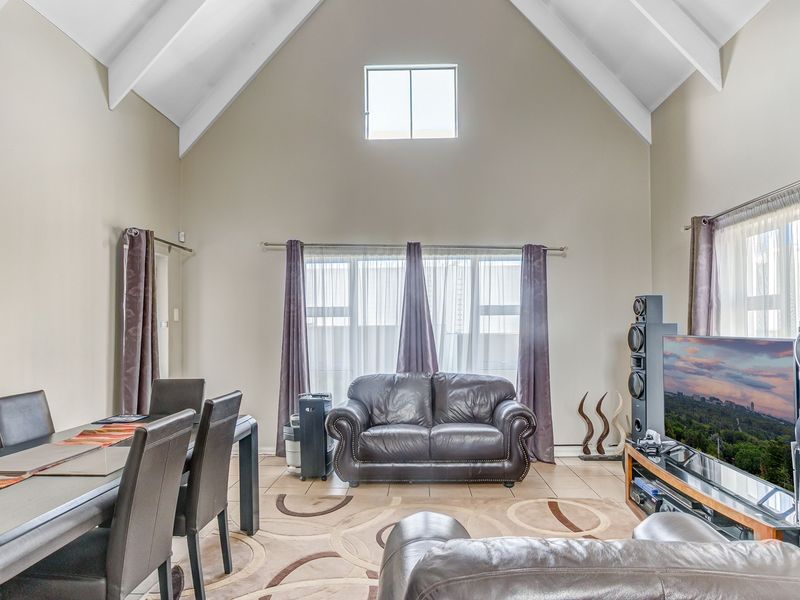 Spacious open-plan living and dining area featuring a high vaulted ceiling, tiled flooring, and a large clerestory window providing ample natural light.