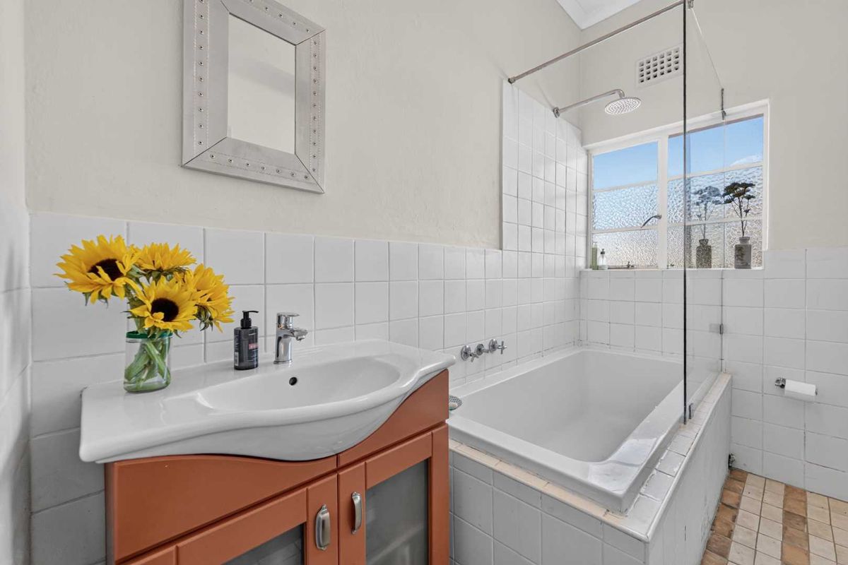 A functional bathroom featuring a built-in bathtub with shower overhead, glass screen, and a vanity unit with a ceramic basin.