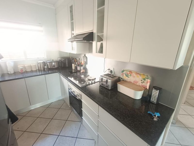 A functional kitchen featuring white cabinetry, dark granite countertops, an integrated electric hob, oven, and extractor fan with tiled flooring.