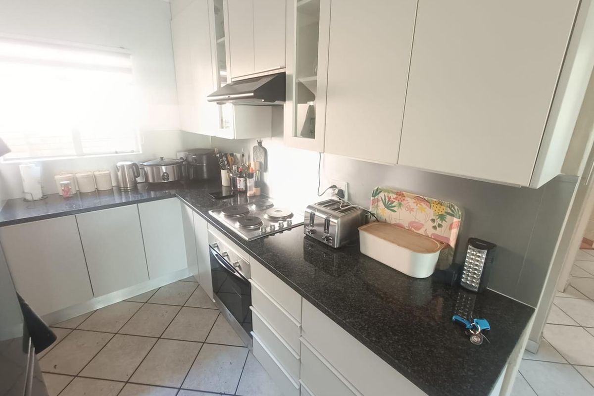 A functional kitchen featuring white cabinetry, dark granite countertops, an integrated electric hob, oven, and extractor fan with tiled flooring.