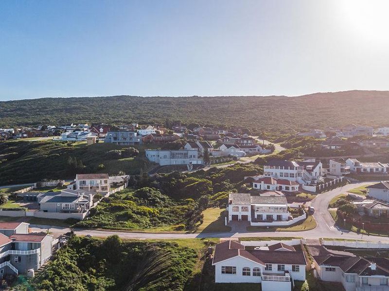An aerial view of a coastal residential neighborhood featuring various houses set against a hilly landscape.
