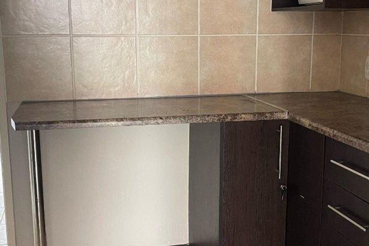 A functional kitchen corner featuring dark wood cabinetry, laminate countertops, and neutral ceramic tile flooring and backsplash.