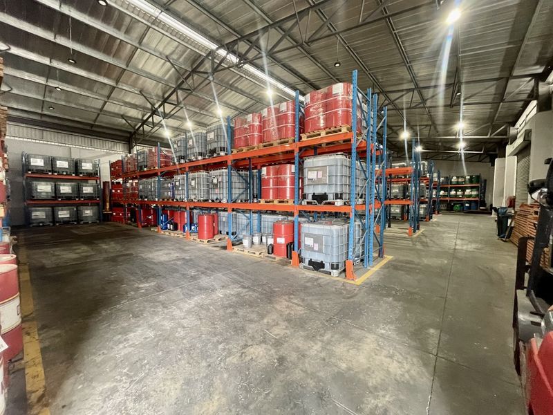 Spacious industrial warehouse featuring high-bay lighting, exposed steel roof trusses, durable concrete flooring, and extensive heavy-duty racking systems for storage.