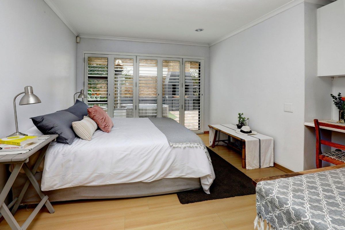 A bedroom featuring light wood-look flooring, white walls, and folding glass doors that provide access to an outdoor patio area.