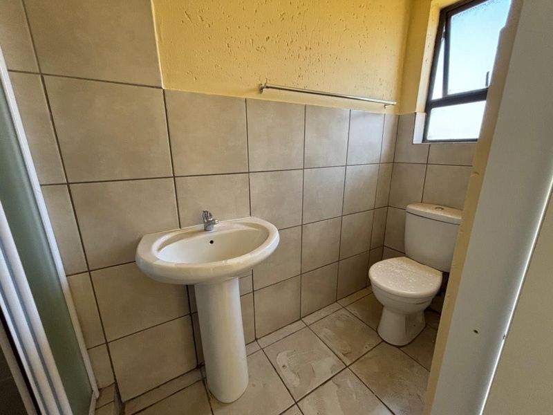 A compact bathroom featuring a pedestal basin, a standard toilet, and neutral wall tiling with a window for natural ventilation.