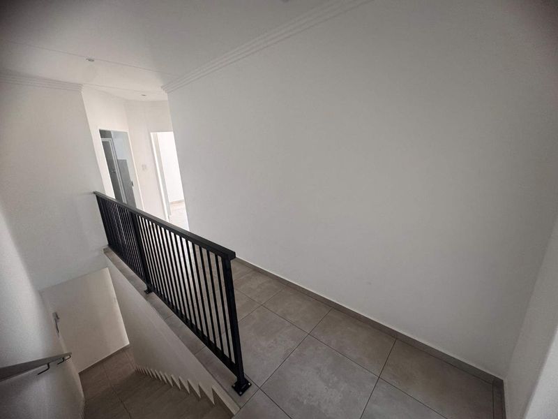 A clean and modern upper-level hallway featuring neutral tiled flooring and a sleek black metal balustrade overlooking the staircase.