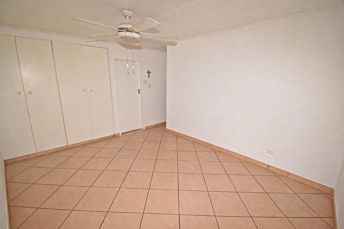 A vacant bedroom featuring tiled flooring, built-in cupboards, and a ceiling fan.