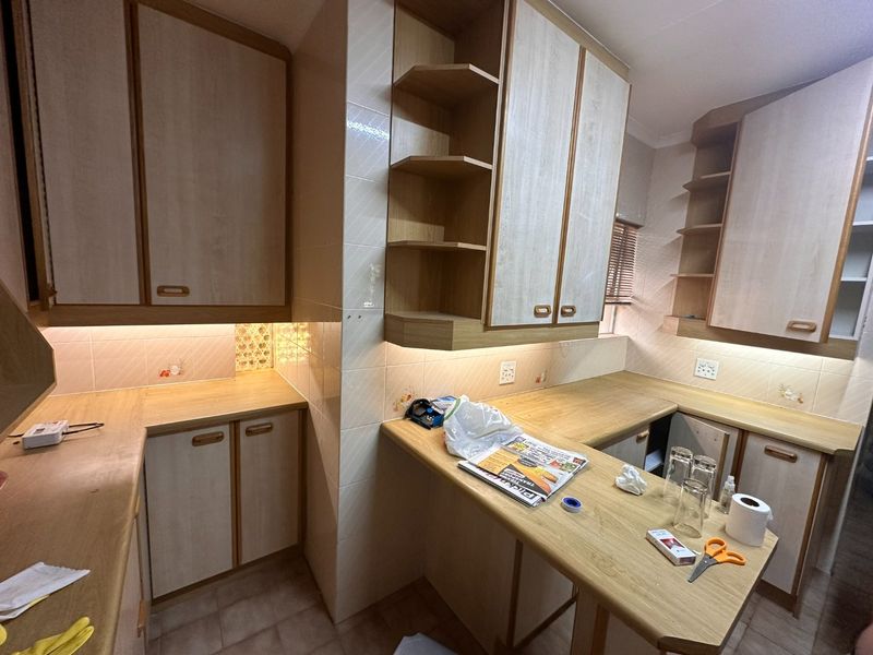 A functional kitchen featuring light wood-tone laminate cabinetry, ample countertop workspace, tiled backsplash, and integrated under-cabinet lighting.