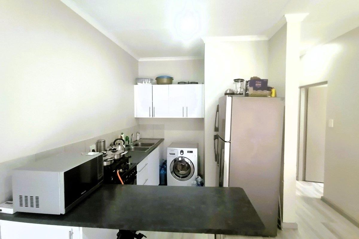 Compact kitchen featuring built-in cabinetry, a stainless steel sink, and space for a washing machine, with a breakfast counter extension.