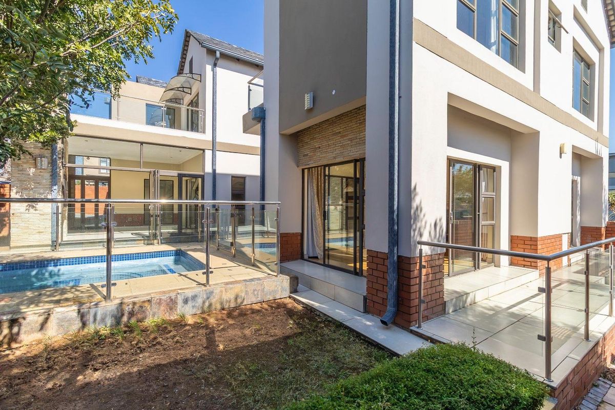 Rear exterior view featuring a swimming pool, tiled patio area, modern glass balustrades, and multi-level architectural design with stone and brick detailing.