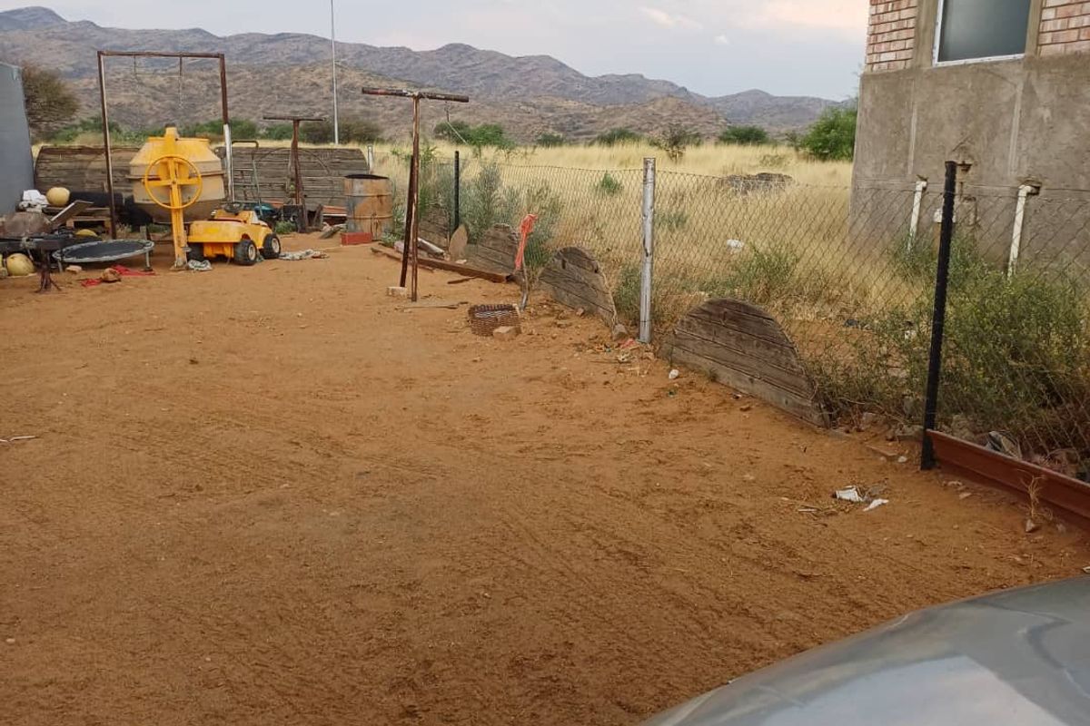Rear exterior view of the property featuring unfinished brickwork, a chain link fence, and an unpaved yard area with mountain views.