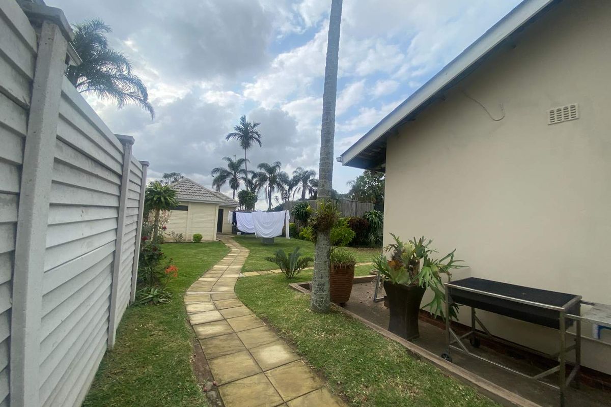 A view of the rear garden featuring a paved walkway, lawn, and boundary wall, leading towards a secondary structure at the back of the property.