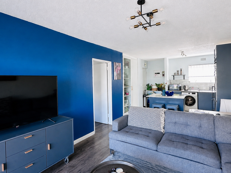 A bright open-plan living and kitchen area featuring a bold blue accent wall, modern cabinetry, and integrated laundry facilities.
