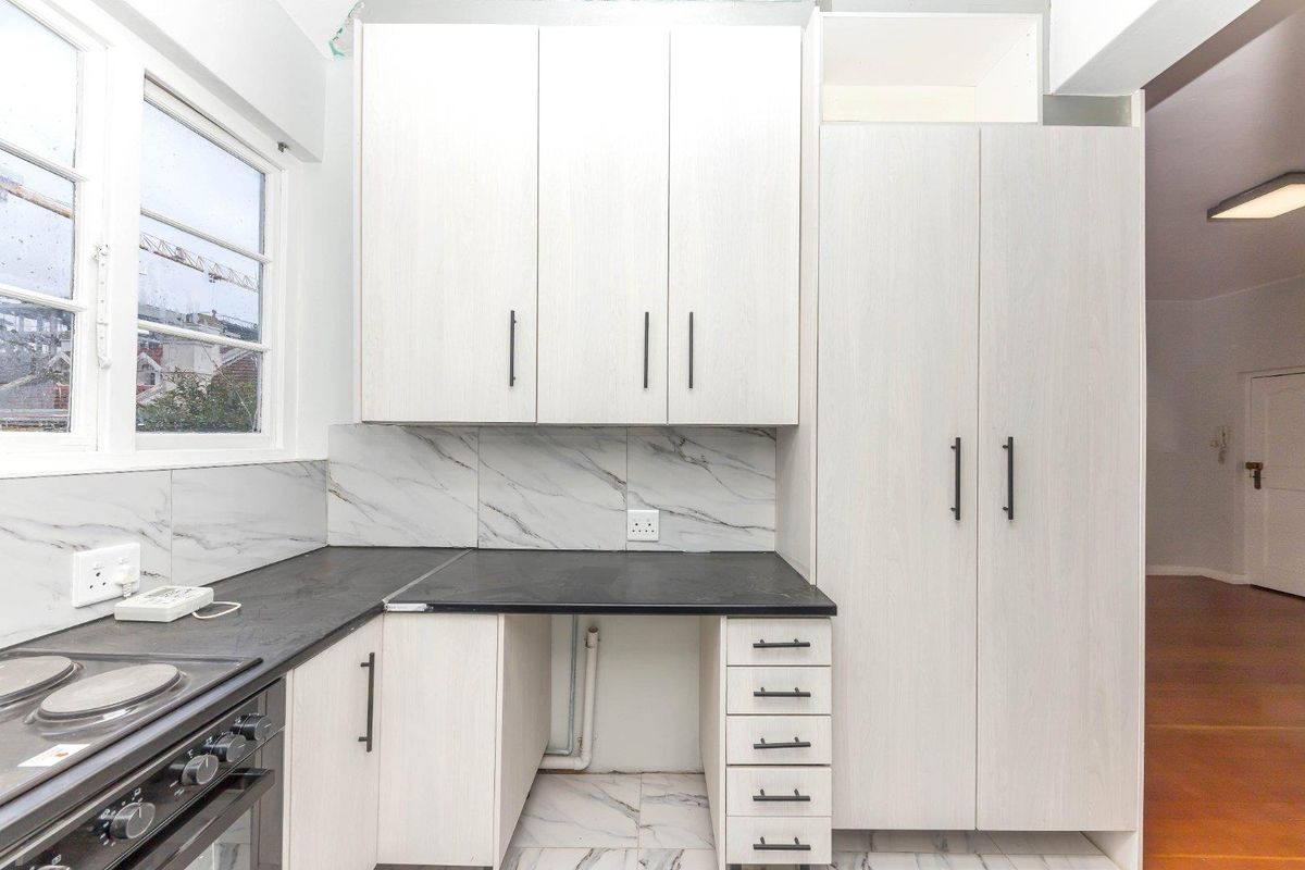 A clean, modern kitchen featuring light wood-grain cabinetry, marble-effect splashbacks, black countertops, and integrated appliance space, presenting a functional and bright culinary area.
