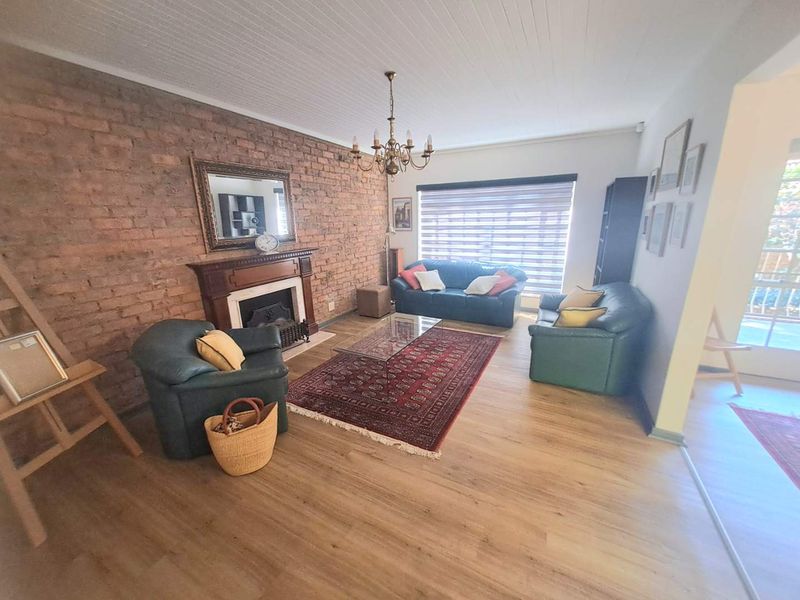 Spacious living room featuring an exposed brick feature wall, a classic fireplace with a timber mantel, and light-toned laminate flooring.