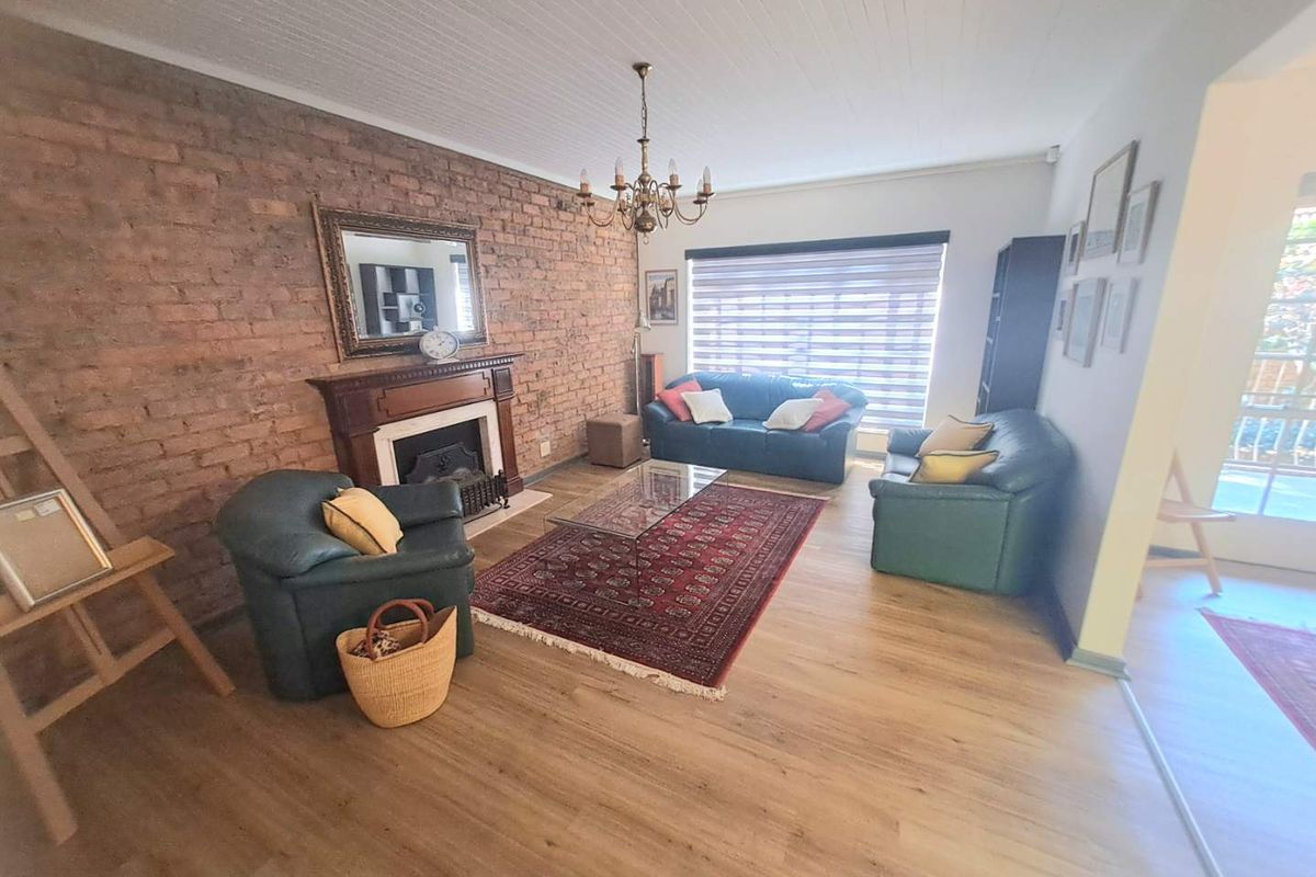 Spacious living room featuring an exposed brick feature wall, a classic fireplace with a timber mantel, and light-toned laminate flooring.