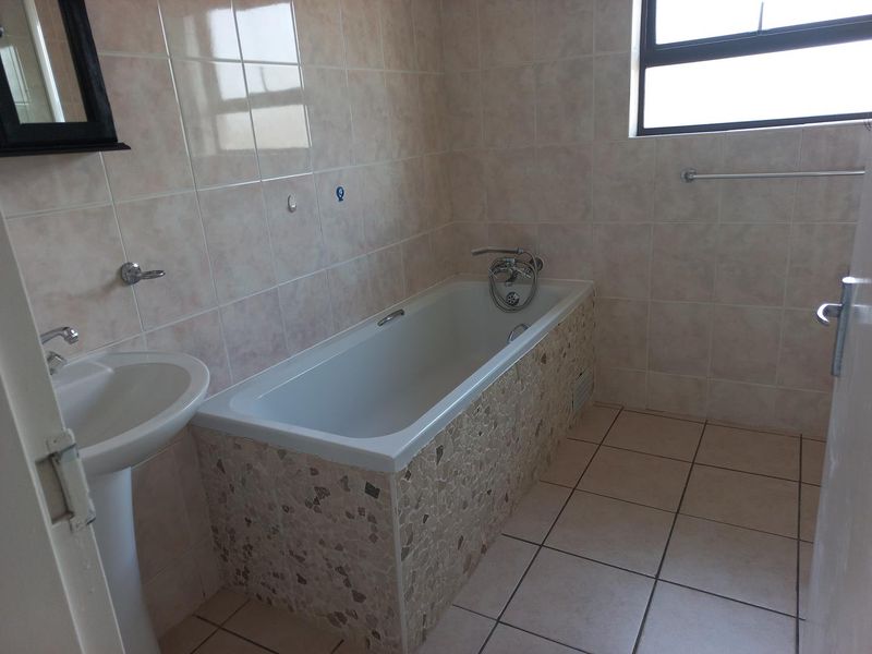 A functional bathroom featuring a pedestal basin, a built-in bathtub with mosaic-style tiling, and neutral ceramic wall and floor tiles.