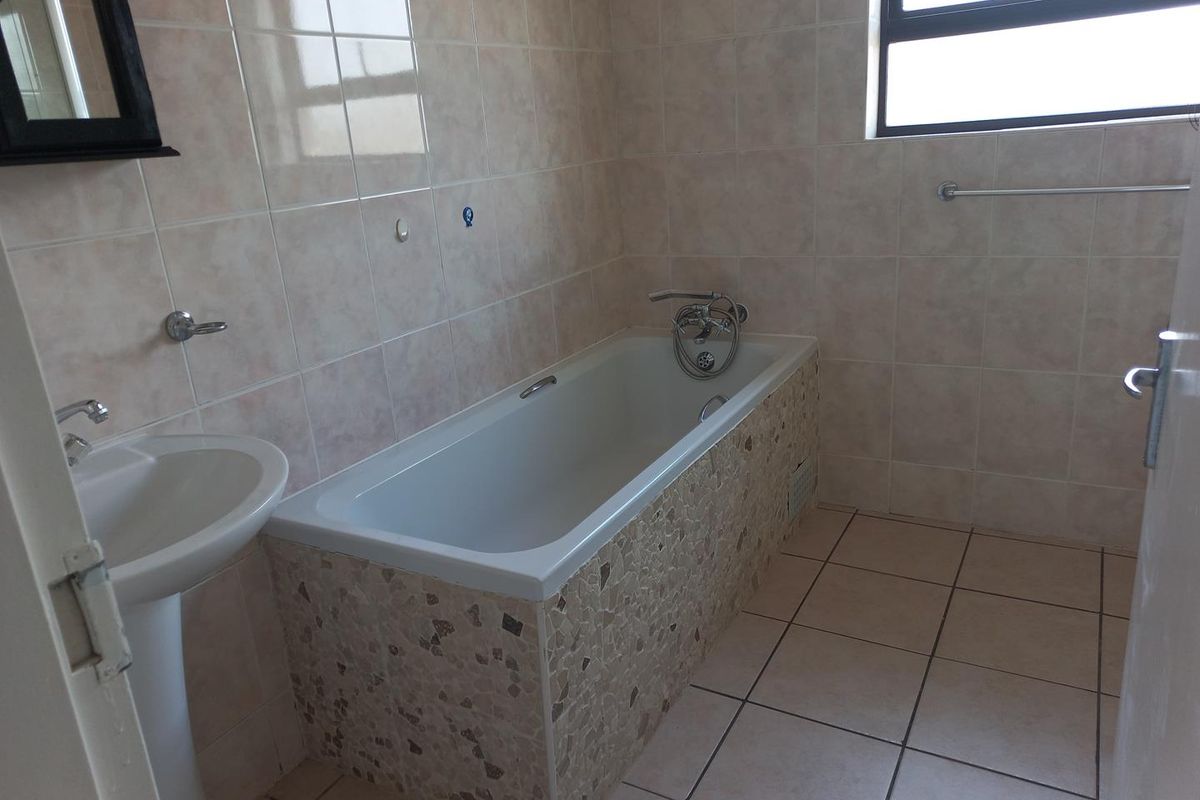 A functional bathroom featuring a pedestal basin, a built-in bathtub with mosaic-style tiling, and neutral ceramic wall and floor tiles.