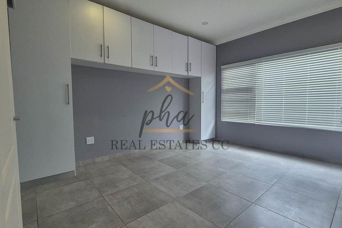 A clean, empty bedroom featuring neutral grey tiled flooring, extensive built-in cabinetry, and fitted venetian blinds.