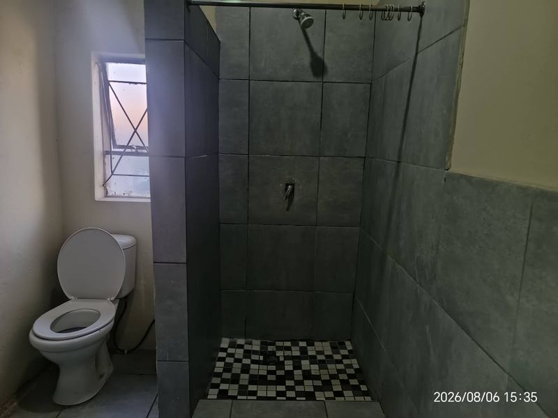 A functional bathroom featuring a tiled shower enclosure and a standard toilet, requiring some maintenance and cosmetic updates.