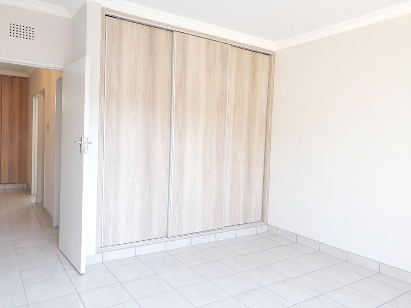 A bright, empty bedroom featuring neutral tiled flooring and modern built-in cupboards with light wood-grain finish.