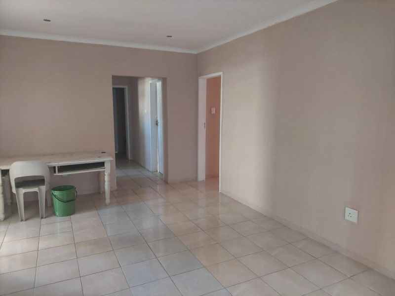 A spacious, neutral-toned living area featuring tiled flooring and recessed downlights, offering a blank canvas for interior design.