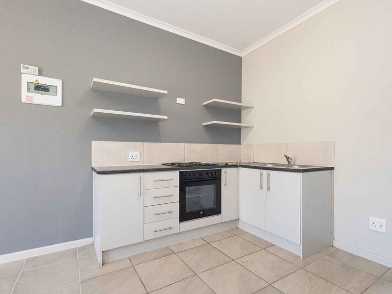 Compact kitchen featuring white cabinetry, built-in oven, gas hob, stainless steel sink, and neutral tiled flooring with a modern grey accent wall.