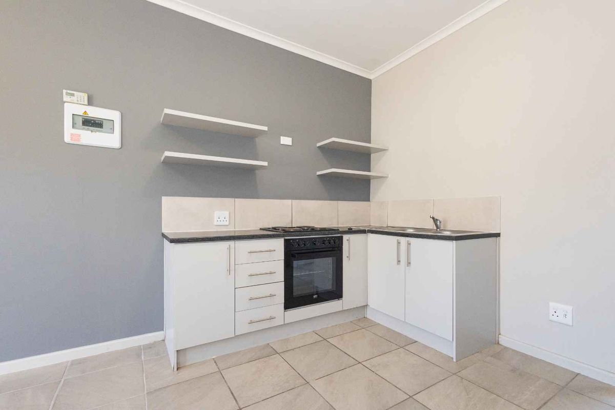 Compact kitchen featuring white cabinetry, built-in oven, gas hob, stainless steel sink, and neutral tiled flooring with a modern grey accent wall.