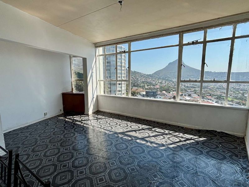 An empty living room featuring large windows with expansive mountain and city views, requiring cosmetic updates to the flooring and ceiling finishes.