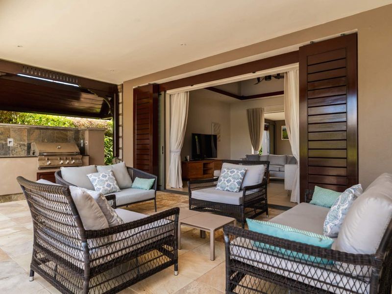 Spacious covered patio featuring a built-in outdoor barbecue station, stone flooring, and large sliding doors providing seamless access to the interior living area.