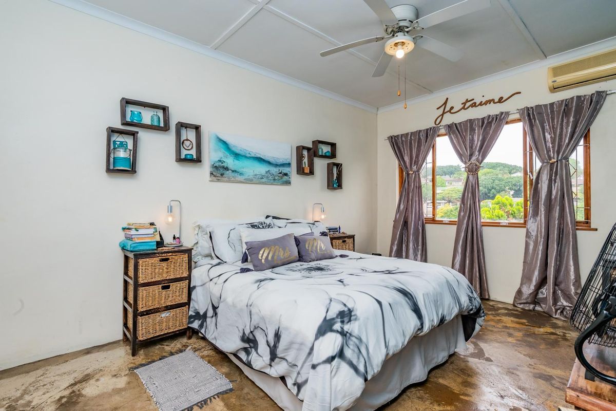A bedroom featuring a ceiling fan, wall-mounted air conditioning unit, and exposed concrete flooring with window security bars.