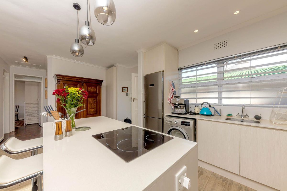 Modern kitchen featuring a central island with an integrated electric hob, stone countertops, stainless steel appliances, and ample cabinetry.