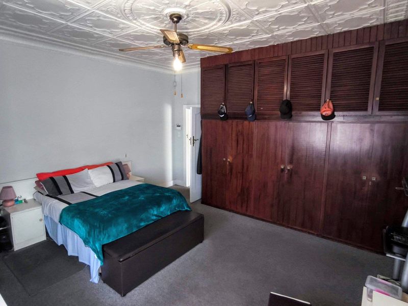 Spacious bedroom featuring extensive built-in wooden cabinetry, a decorative pressed metal ceiling, and a central ceiling fan.