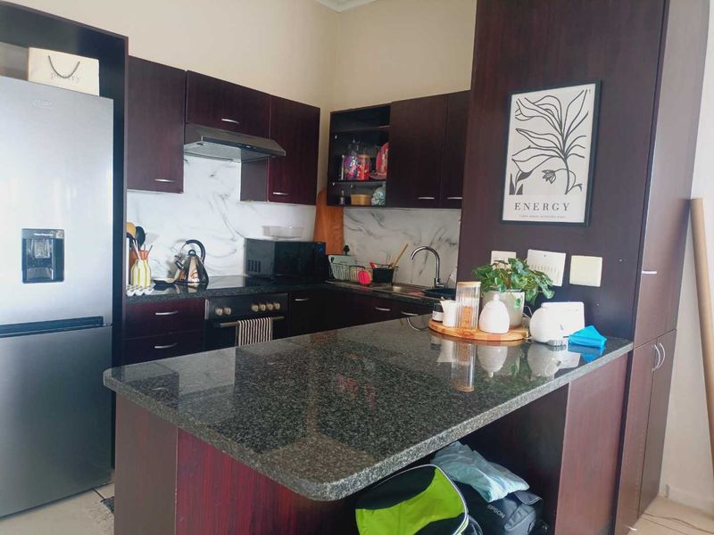 A functional kitchen featuring dark wood cabinetry, granite countertops, a marble-look backsplash, and a convenient breakfast bar for casual dining.