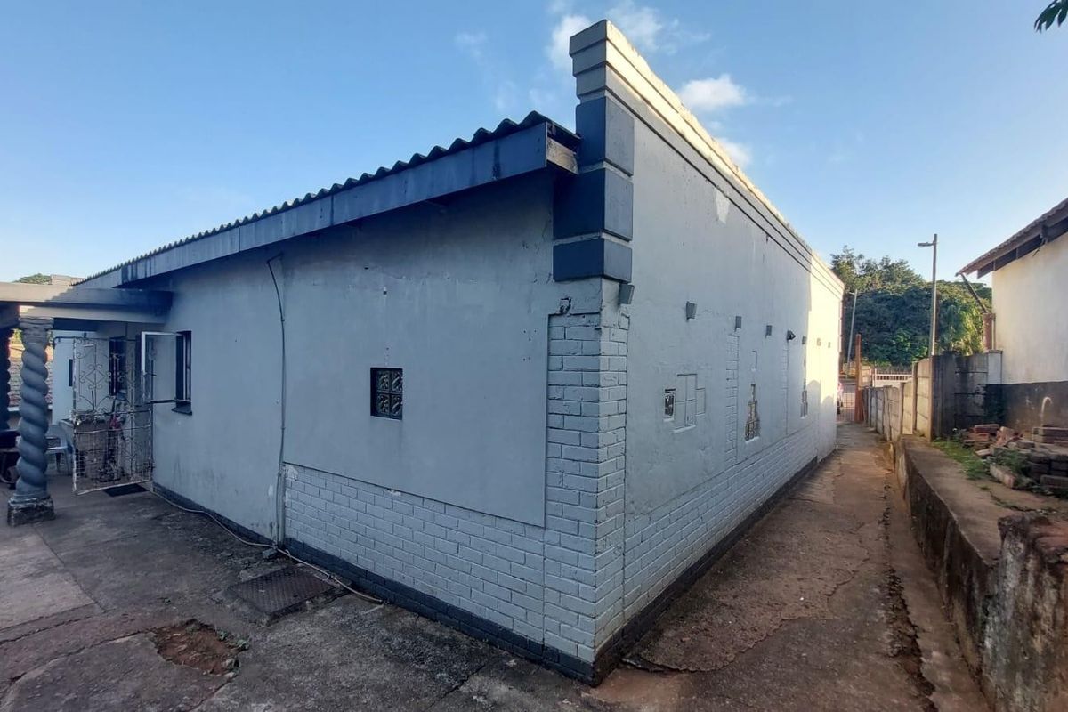 Rear exterior view of the property showing the side facade, concrete driveway, and basic masonry structure with a corrugated metal roof.