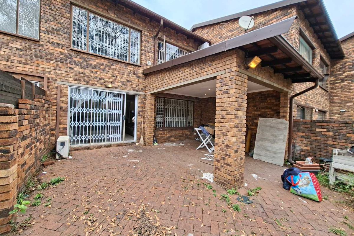 Rear exterior view of a townhouse featuring a covered brick patio area, paved courtyard, and secure window bars.