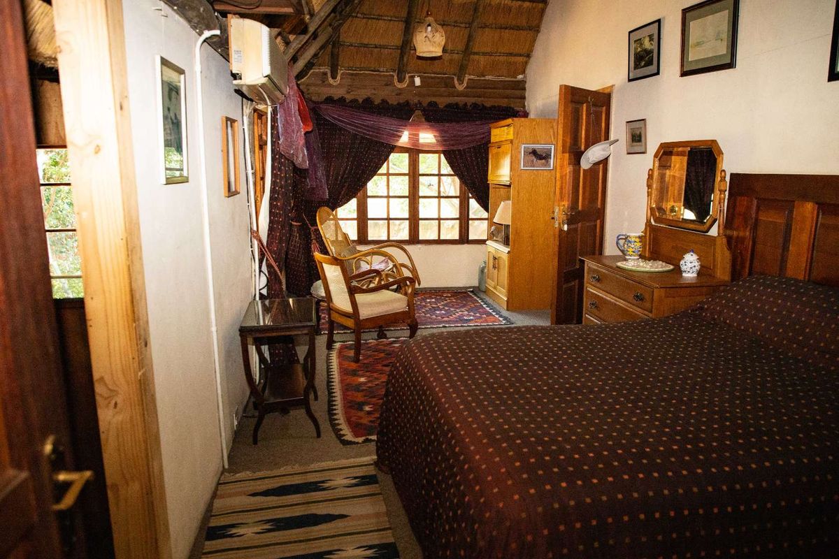 A cozy bedroom featuring a traditional thatched roof, exposed timber beams, and a window with natural light.